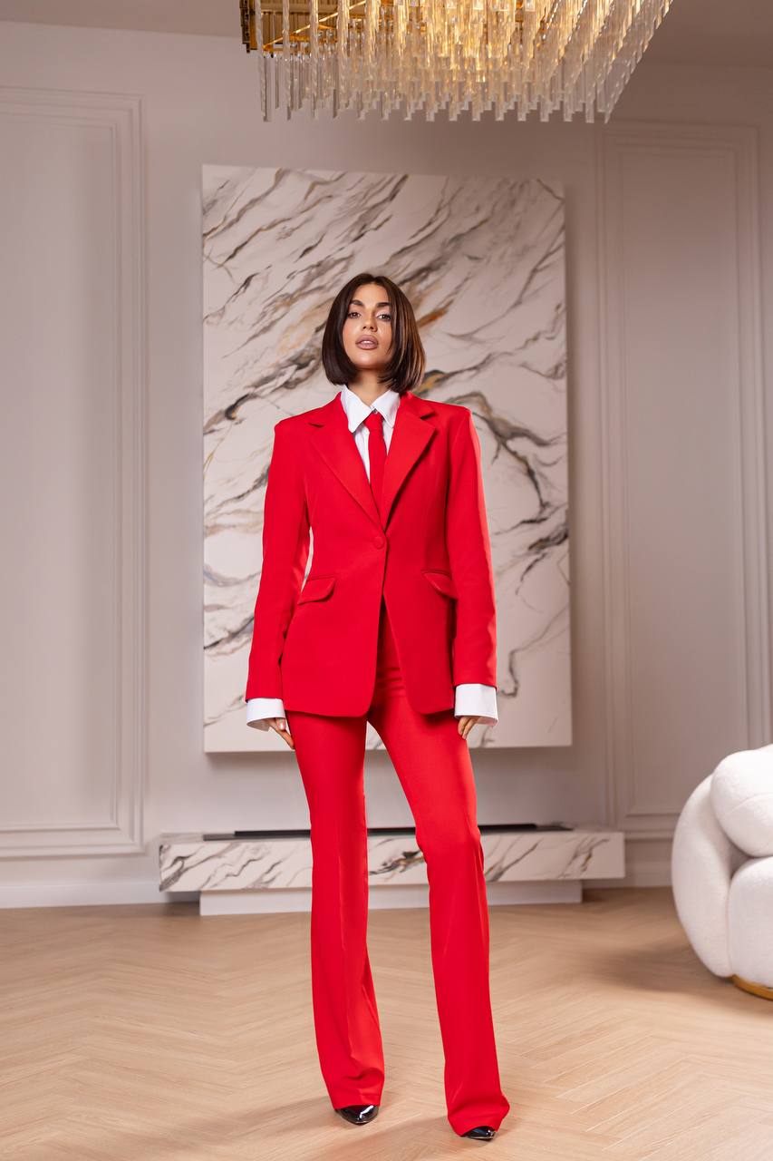 Woman in a red suit standing in a stylish room with marble wall art and chandelier.