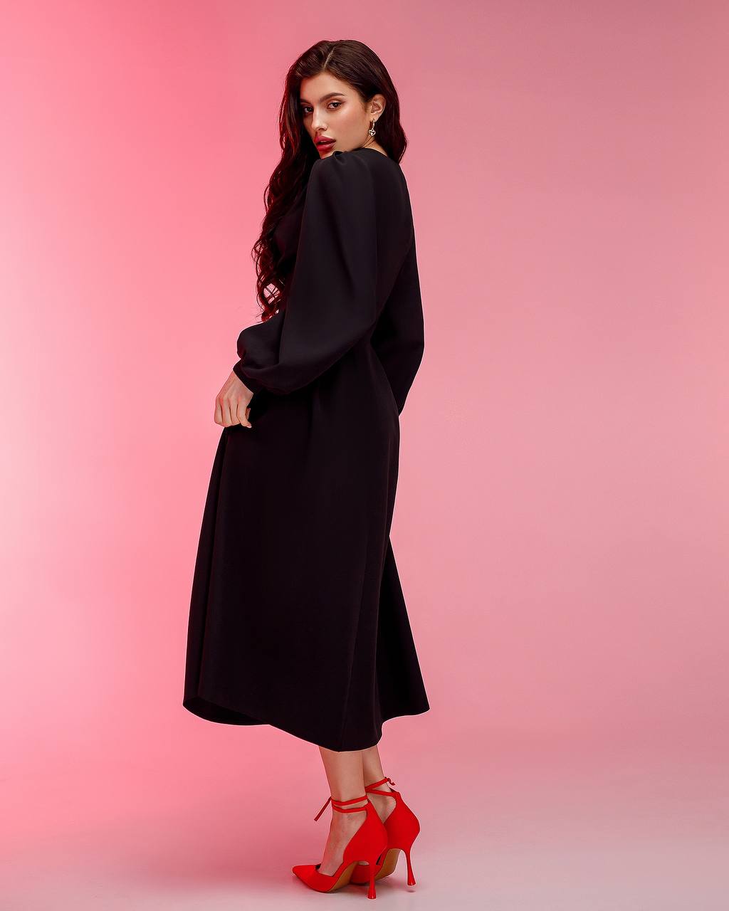 Woman in a black dress with red shoes on a pink background
