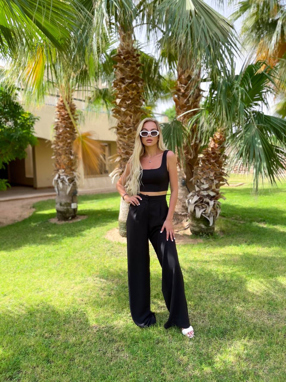 Woman in black outfit standing in a grassy area with palm trees
