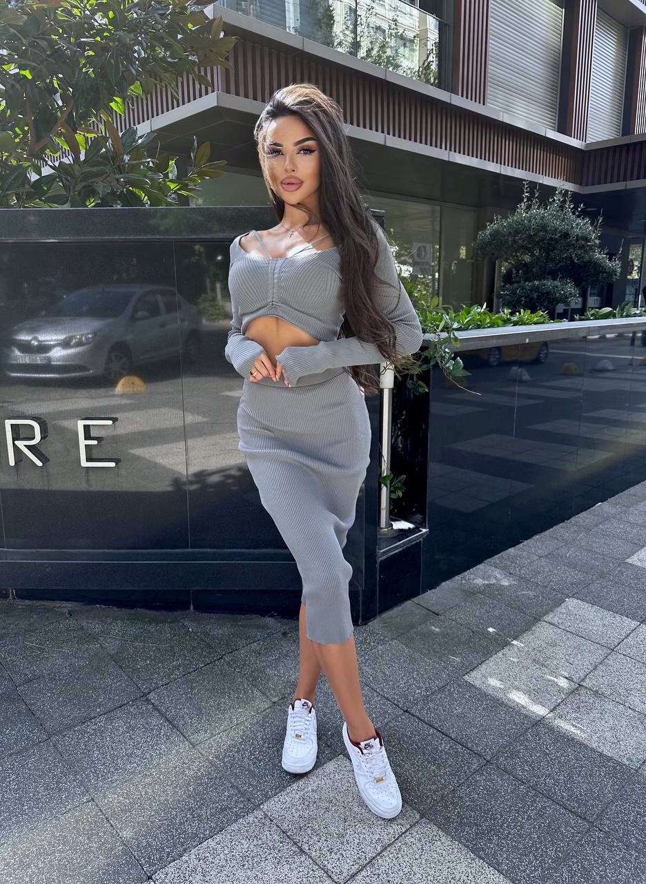 Woman in a gray outfit standing in front of a building entrance.