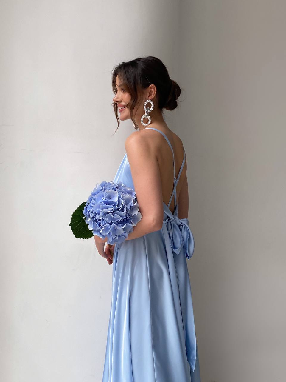 Woman in a light blue dress holding a bouquet of flowers against a plain background