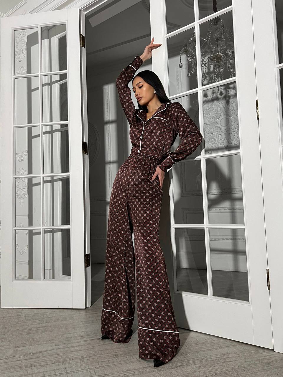 Woman wearing a brown polka dot pajama set standing in front of glass doors.