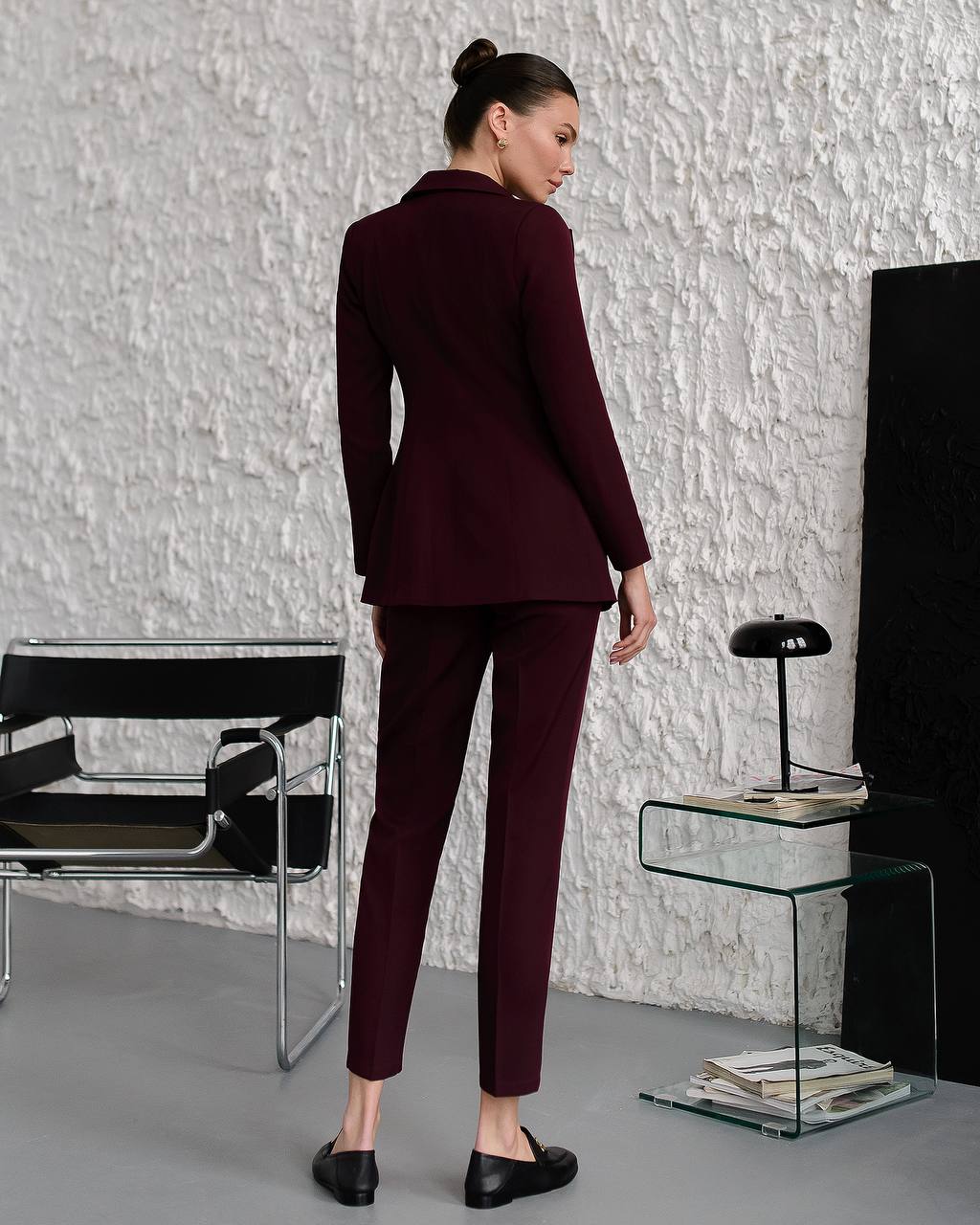 Woman in a burgundy suit standing in a modern room with a textured wall.