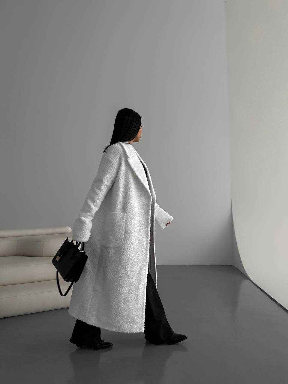 Person wearing a long white coat in a minimalistic setting
