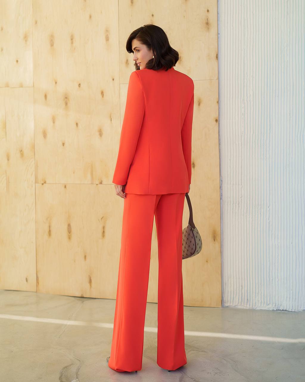 Woman in a red suit standing against a wooden wall.