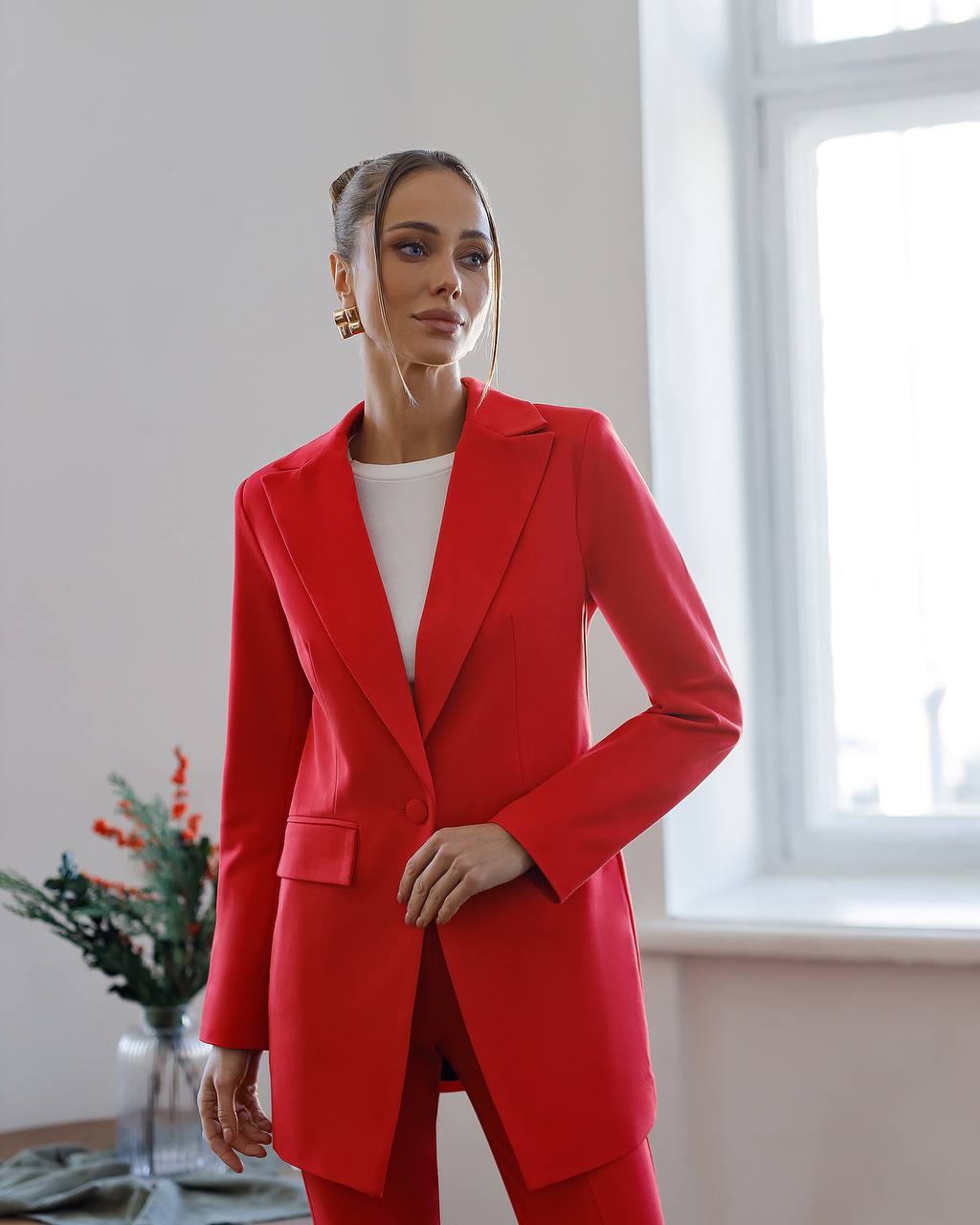 Woman wearing a red suit standing in a room with a window and plant.