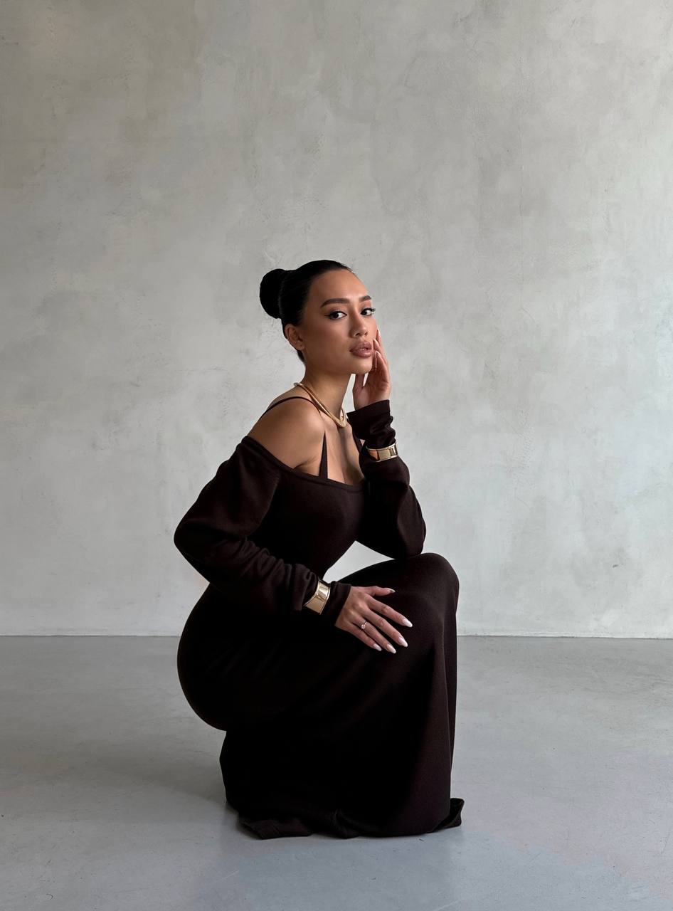 Woman in a dark brown off-shoulder dress sitting against a plain background