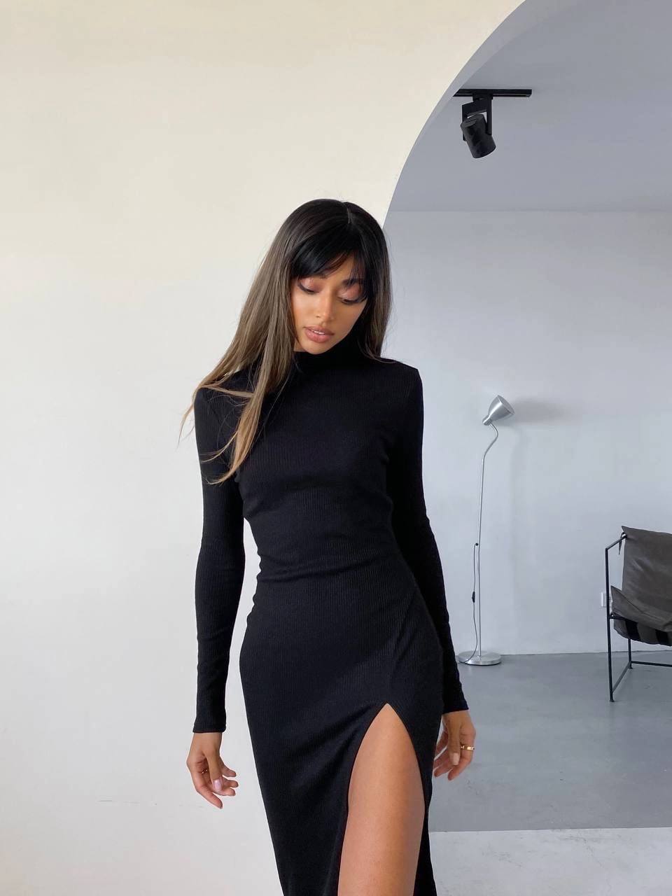 Woman wearing a black long-sleeve dress with a slit in a minimalistic setting