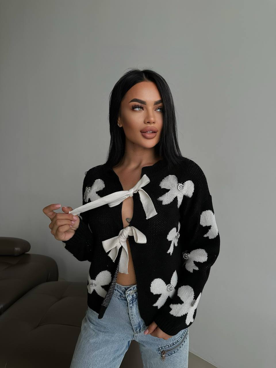 Woman wearing a black cardigan with white floral patterns and light blue jeans.