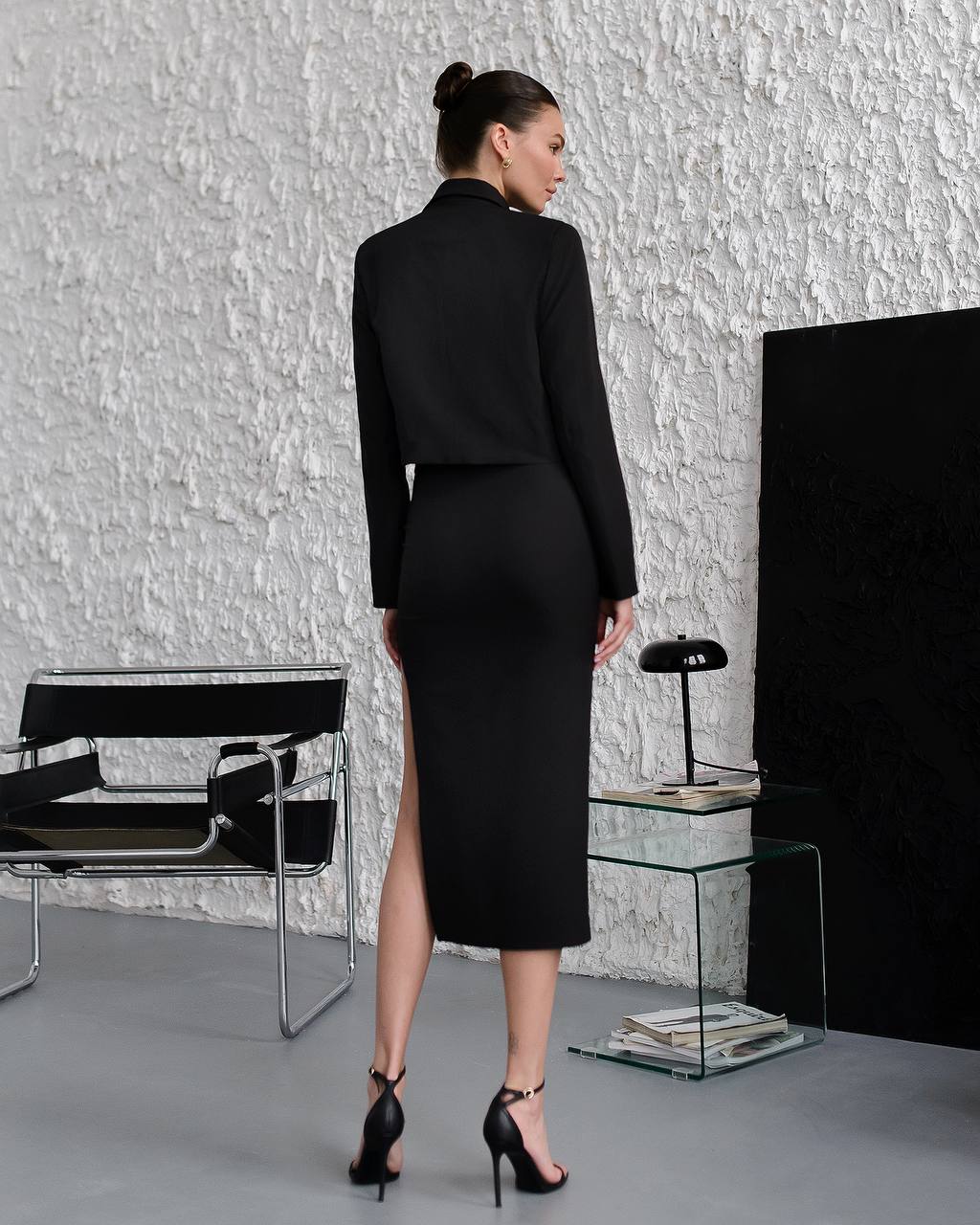 Woman in a black outfit standing in a modern room with minimal decor.