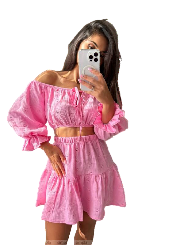 Woman wearing a pink off-shoulder top and skirt set, holding a phone with a white background.
