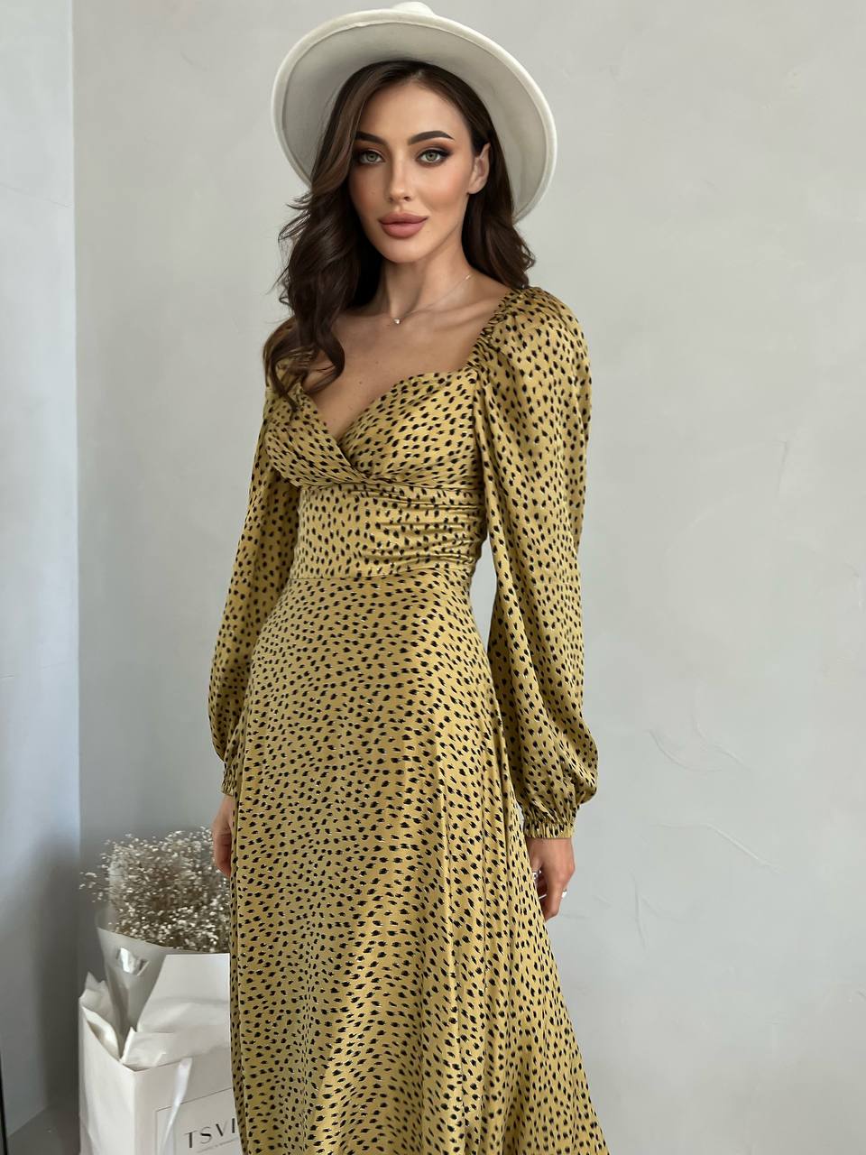Woman wearing a gold leopard print dress and white hat against a plain background
