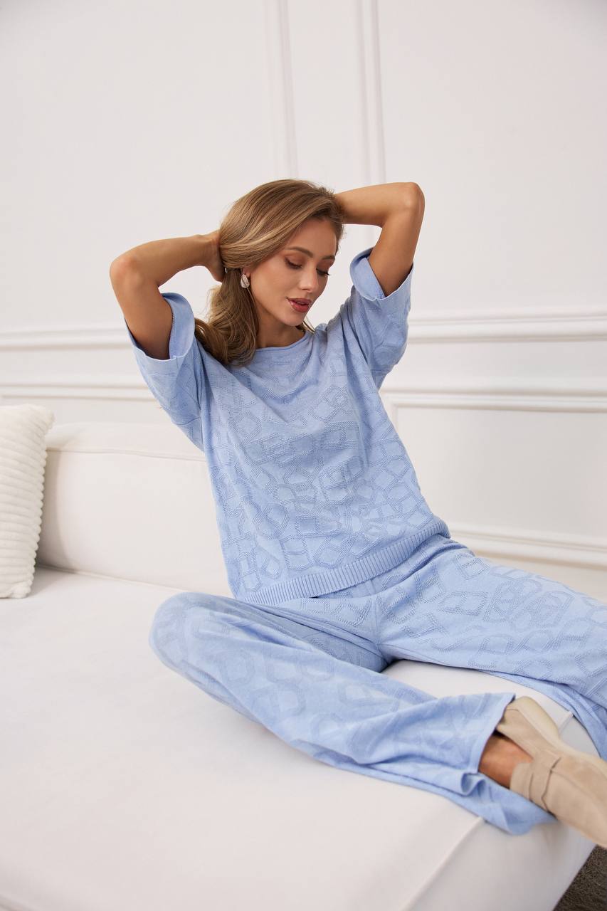 Woman wearing a light blue sweater and pants sitting on a white couch.