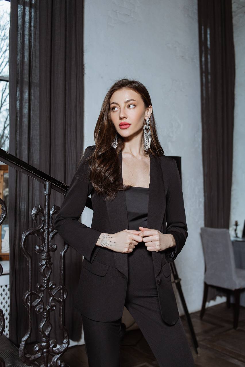 Woman in a black suit standing in an indoor setting with a neutral background