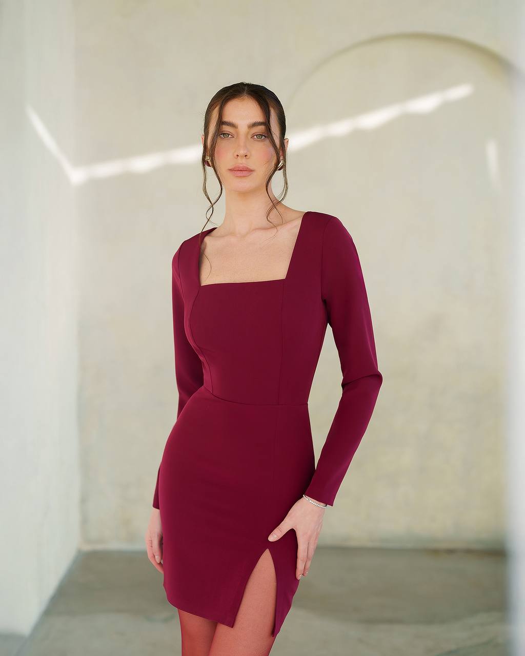 Woman wearing a burgundy dress with a square neckline and long sleeves against a neutral background