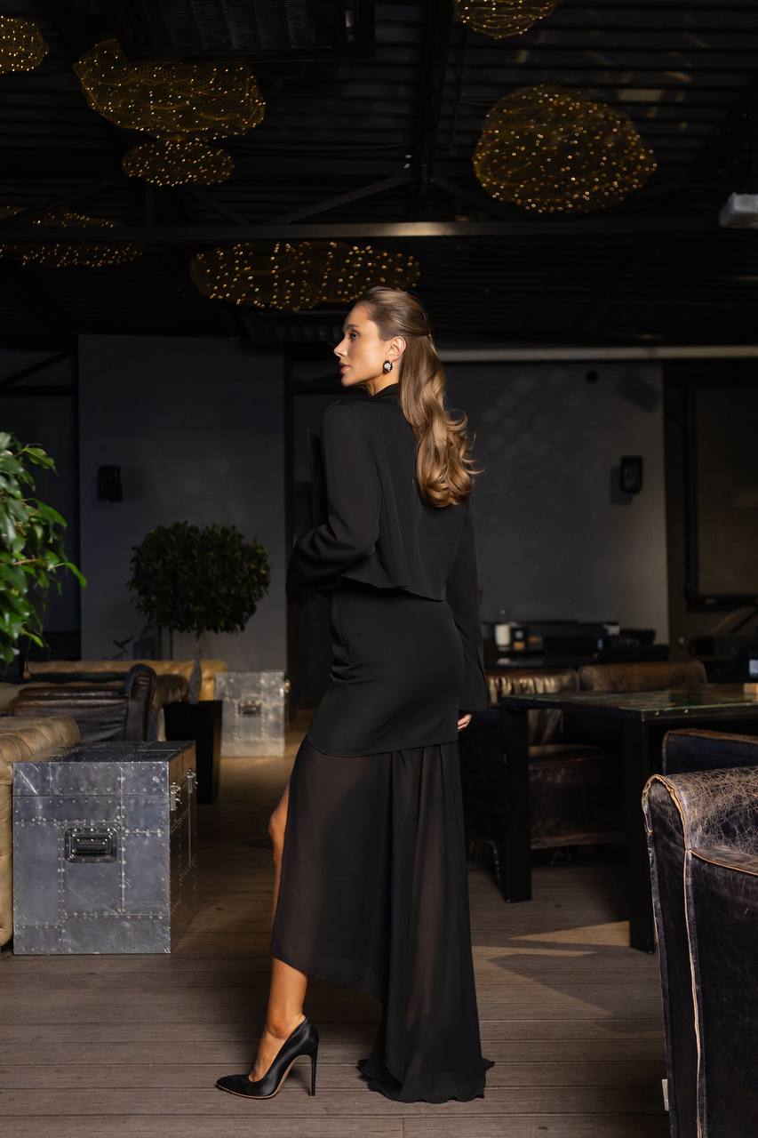 Woman in a black dress standing in a dimly lit room with decorative elements.