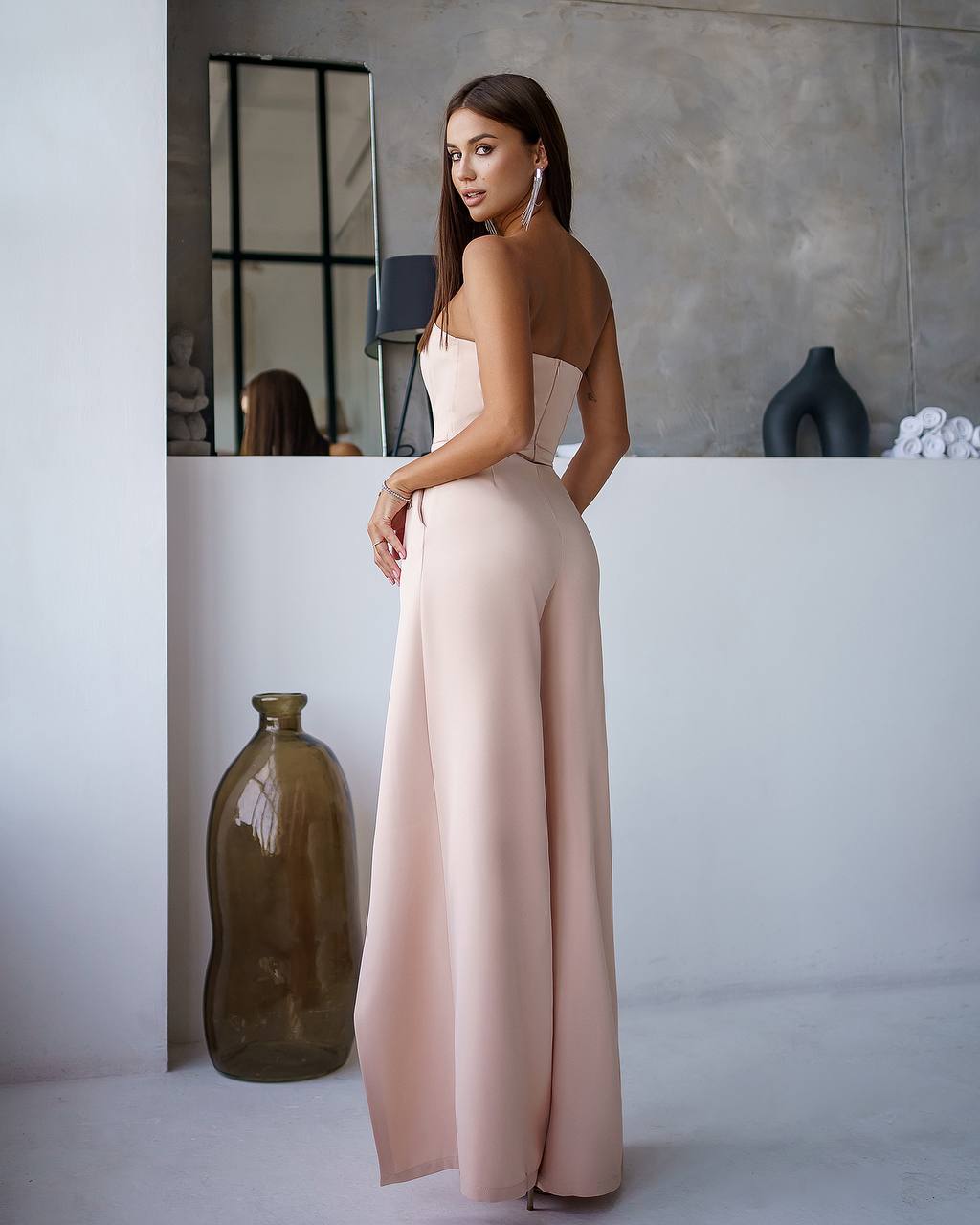 Woman in a pink dress standing in a modern interior setting with vases.
