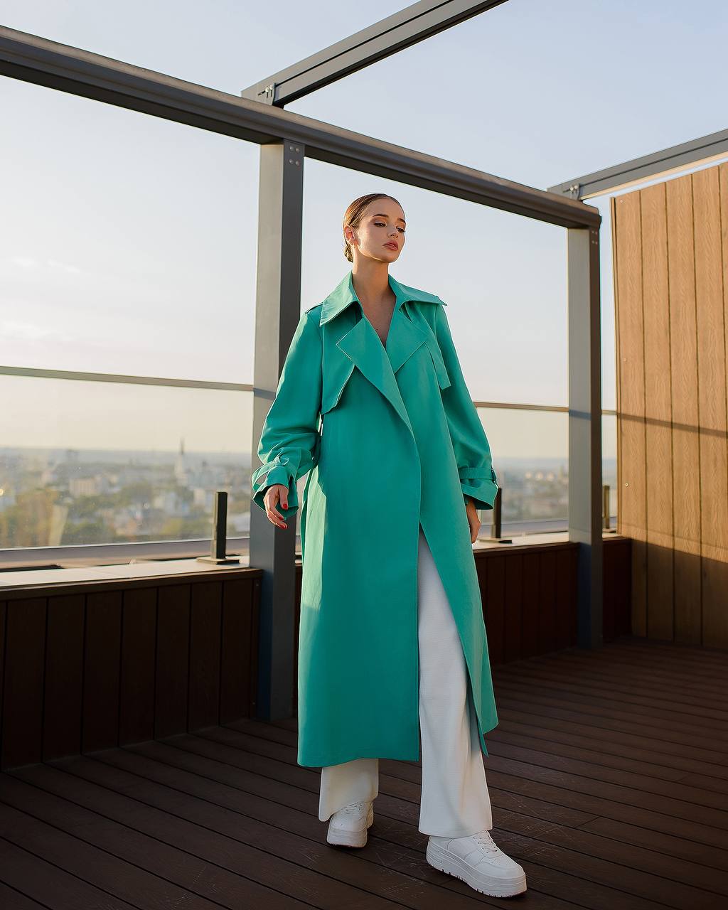 Woman wearing a teal coat on a rooftop with a cityscape view