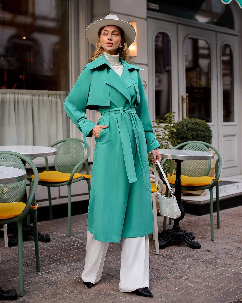Woman in a teal trench coat standing in an outdoor cafe setting