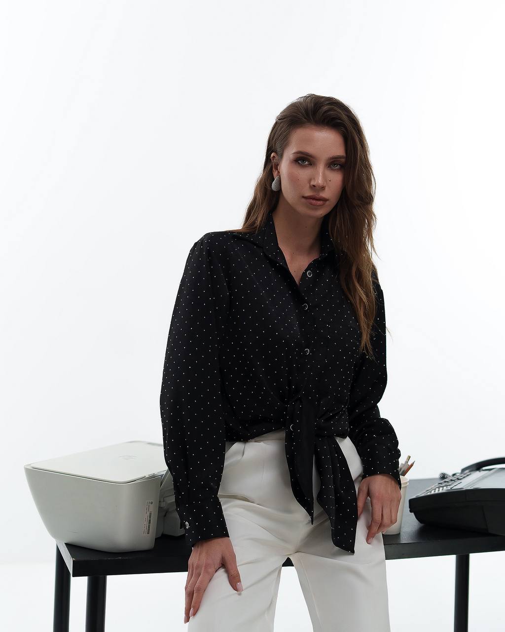 Woman wearing a black patterned shirt and white pants in an office setting