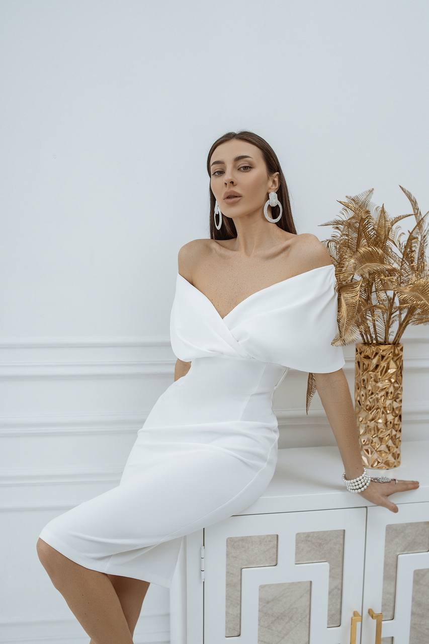 Woman in a white off-shoulder dress posing with a decorative vase against a light background