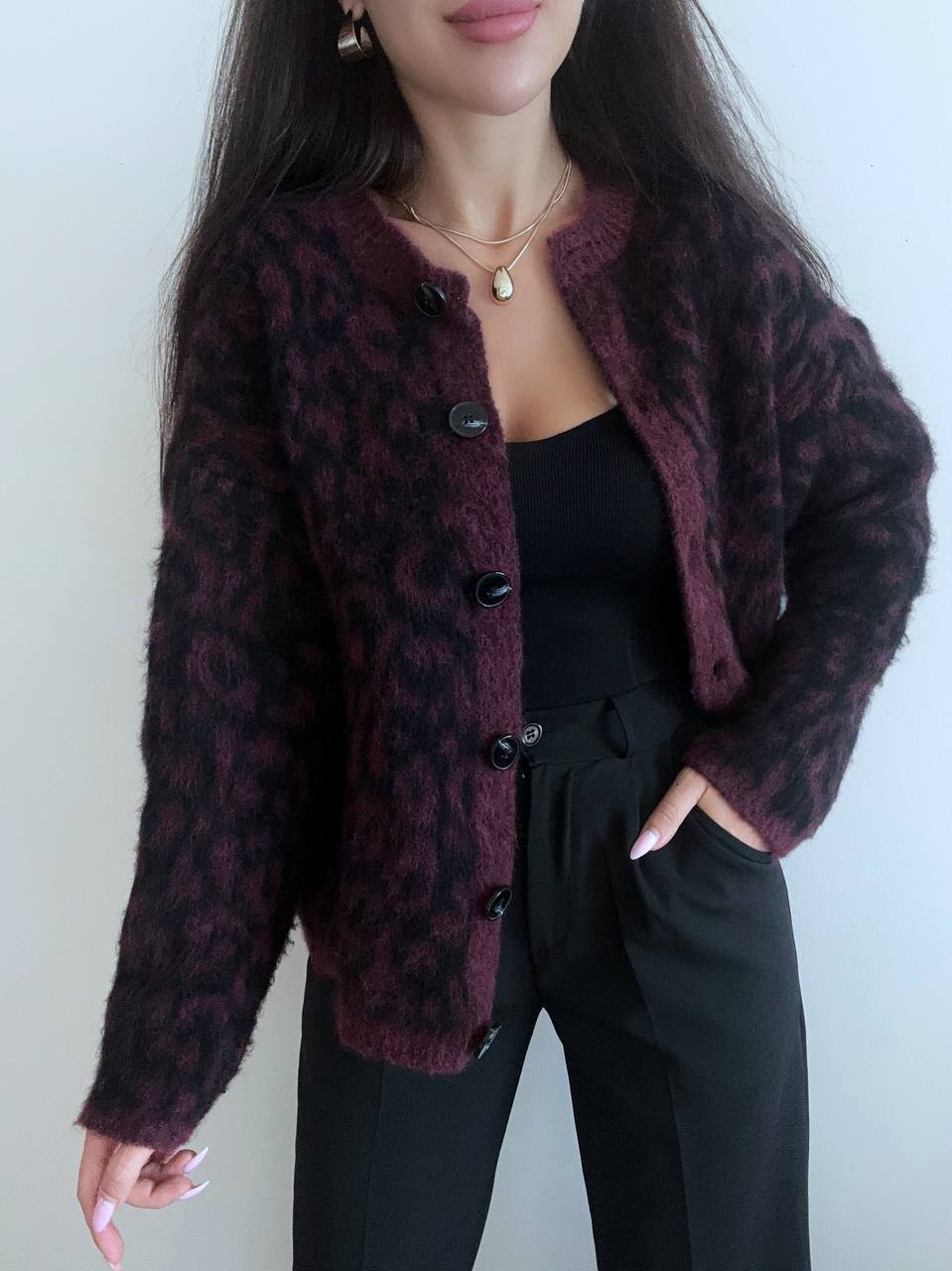 Person wearing a dark purple leopard print cardigan over a black top and pants against a white background