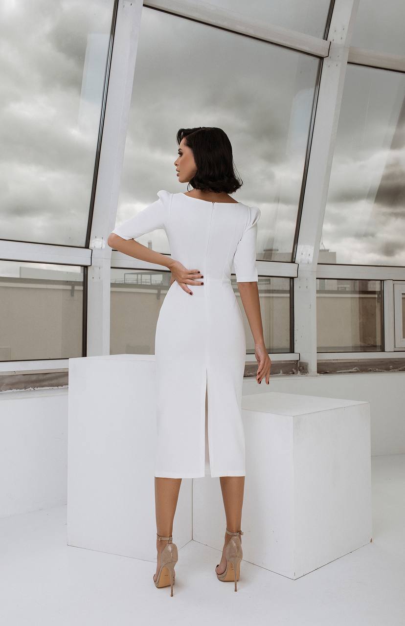 Woman in a white dress standing in a modern indoor setting with large windows.