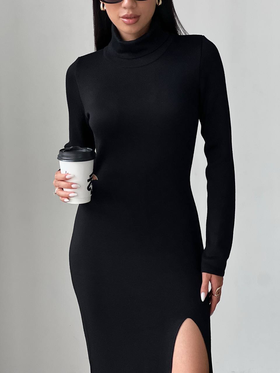 Person wearing a black dress holding a coffee cup against a gray background