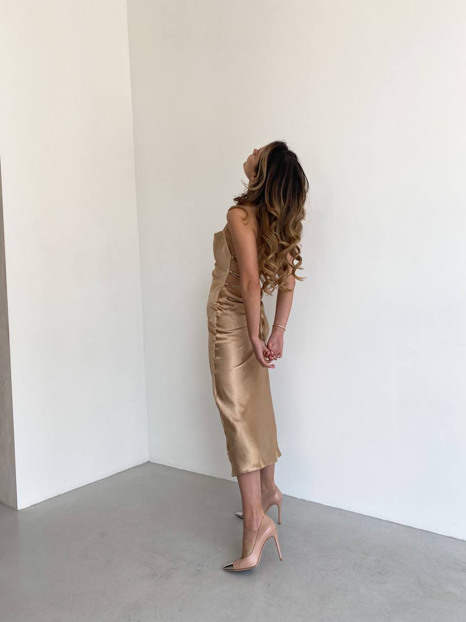 Woman in a gold dress standing against a white wall