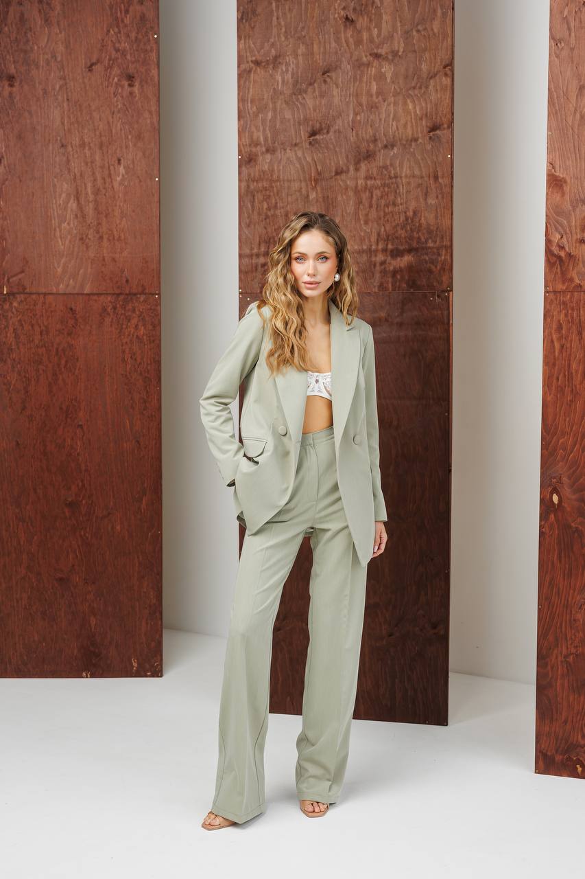 Woman in a light green suit standing against a wooden background