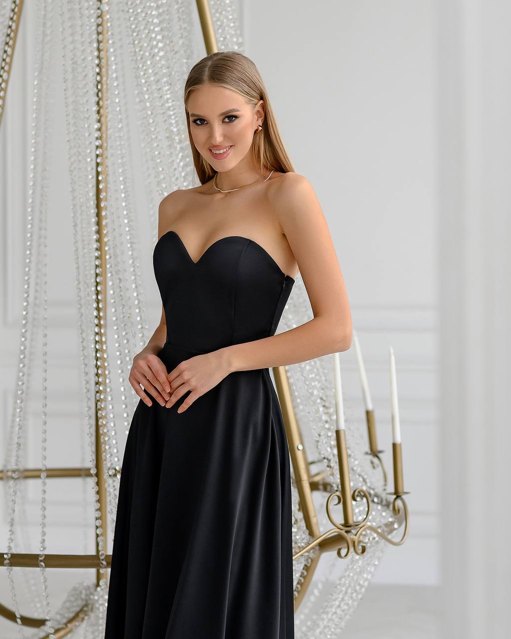 Woman wearing a black strapless dress in a decorative setting with candles and a chandelier.