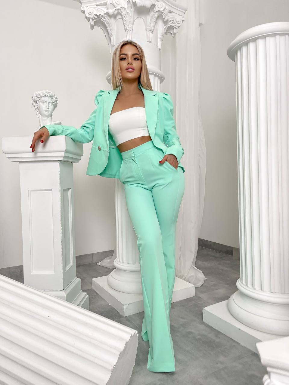 Woman in mint green outfit standing in a classical setting with columns.