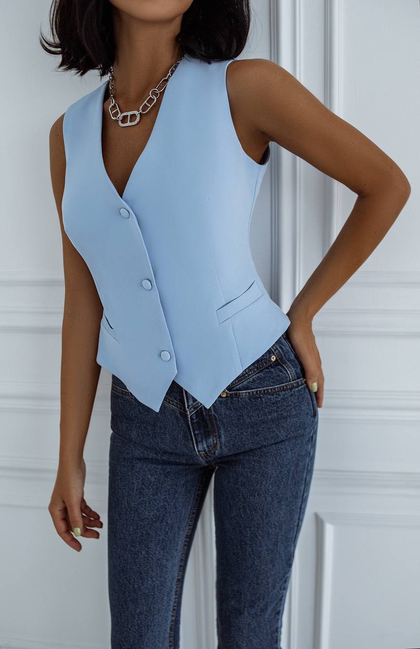 Person wearing a light blue vest over a white top with dark jeans against a white background