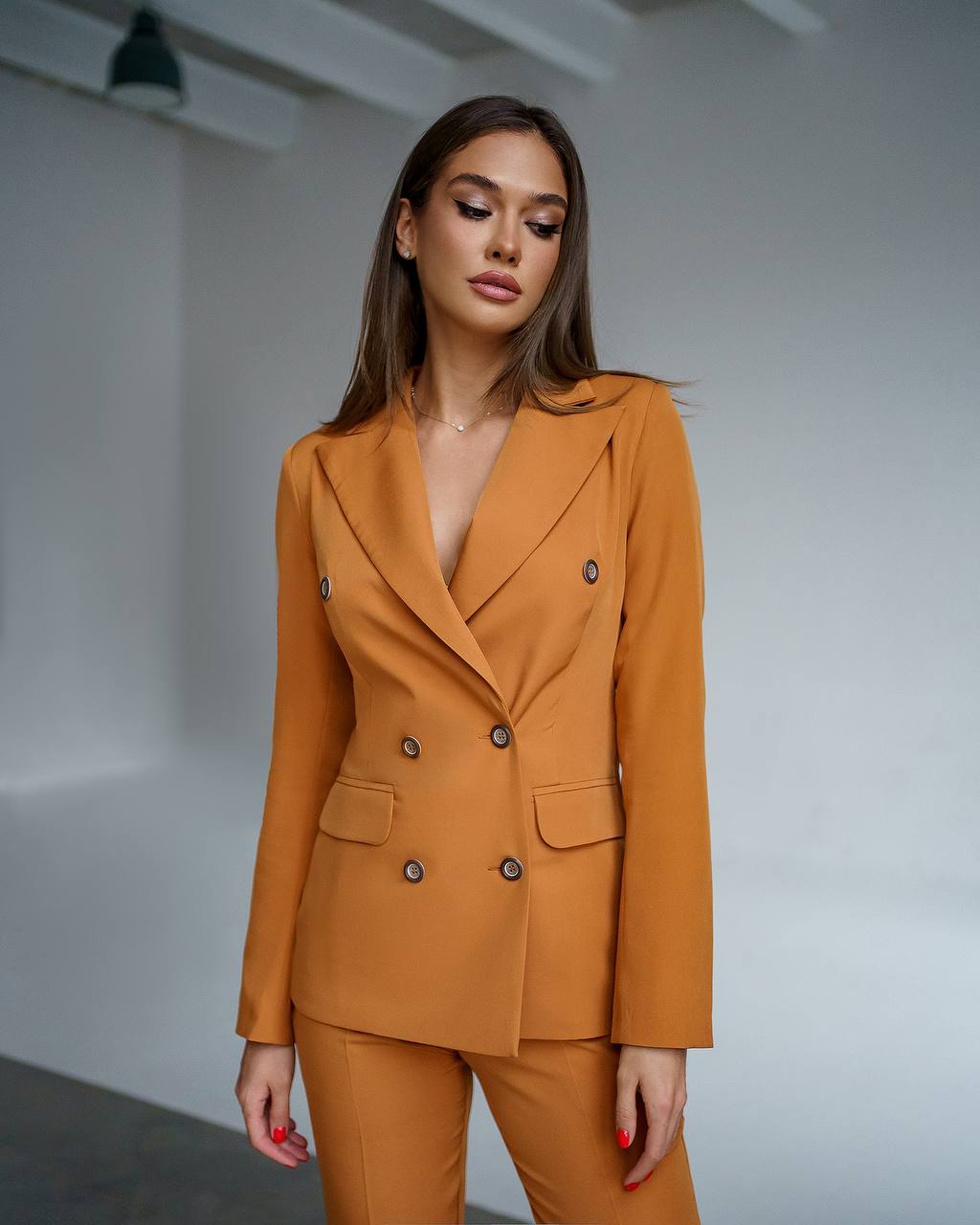 Woman wearing a mustard yellow suit against a plain background