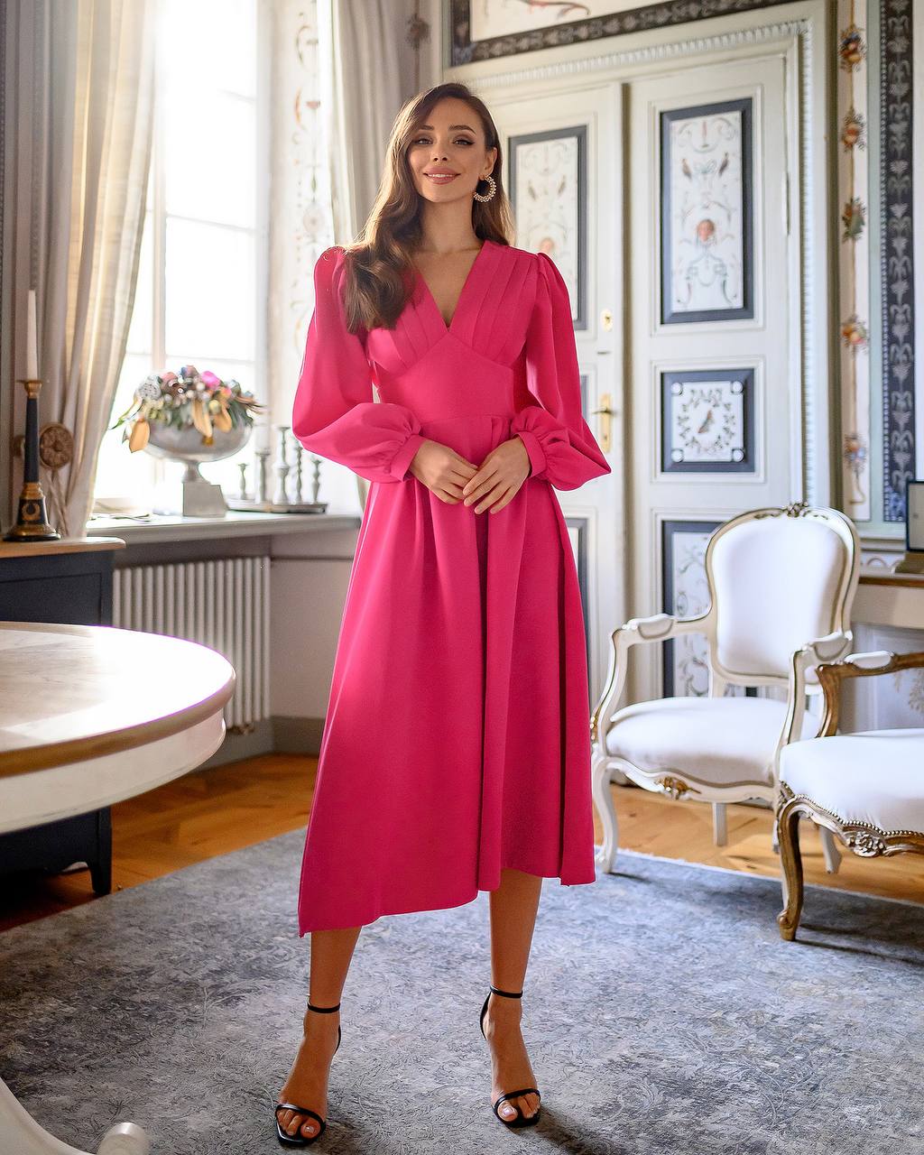 Woman in a pink dress standing in an elegant room with classical decor.