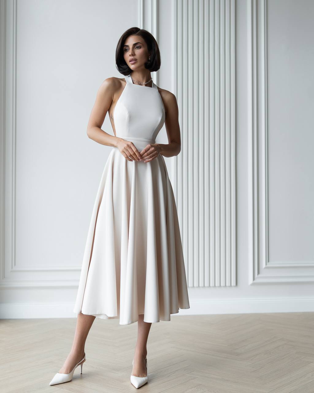 Woman wearing a white dress with a beige skirt against a light-colored wall.