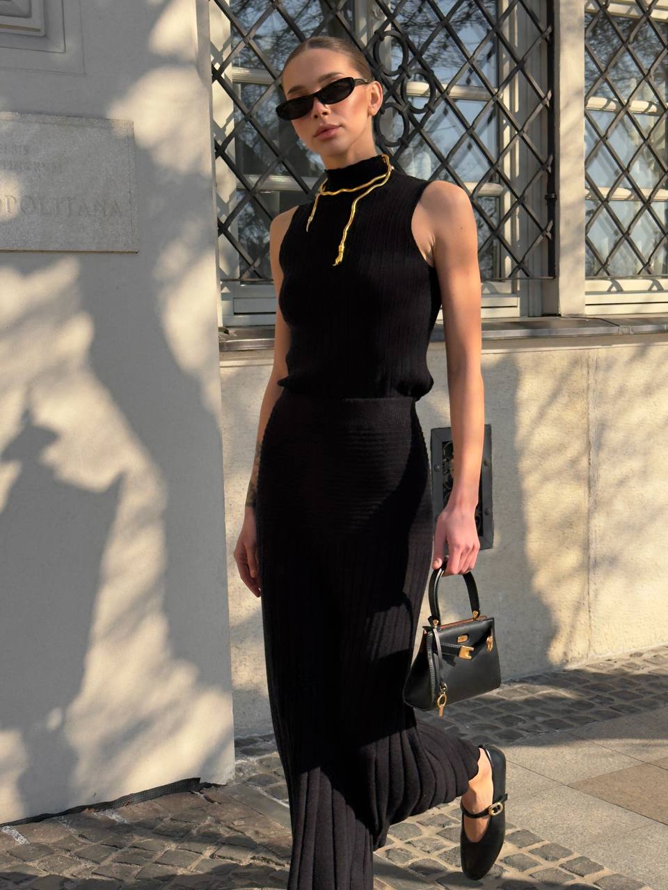Woman in a black dress with a gold necklace walking outdoors.