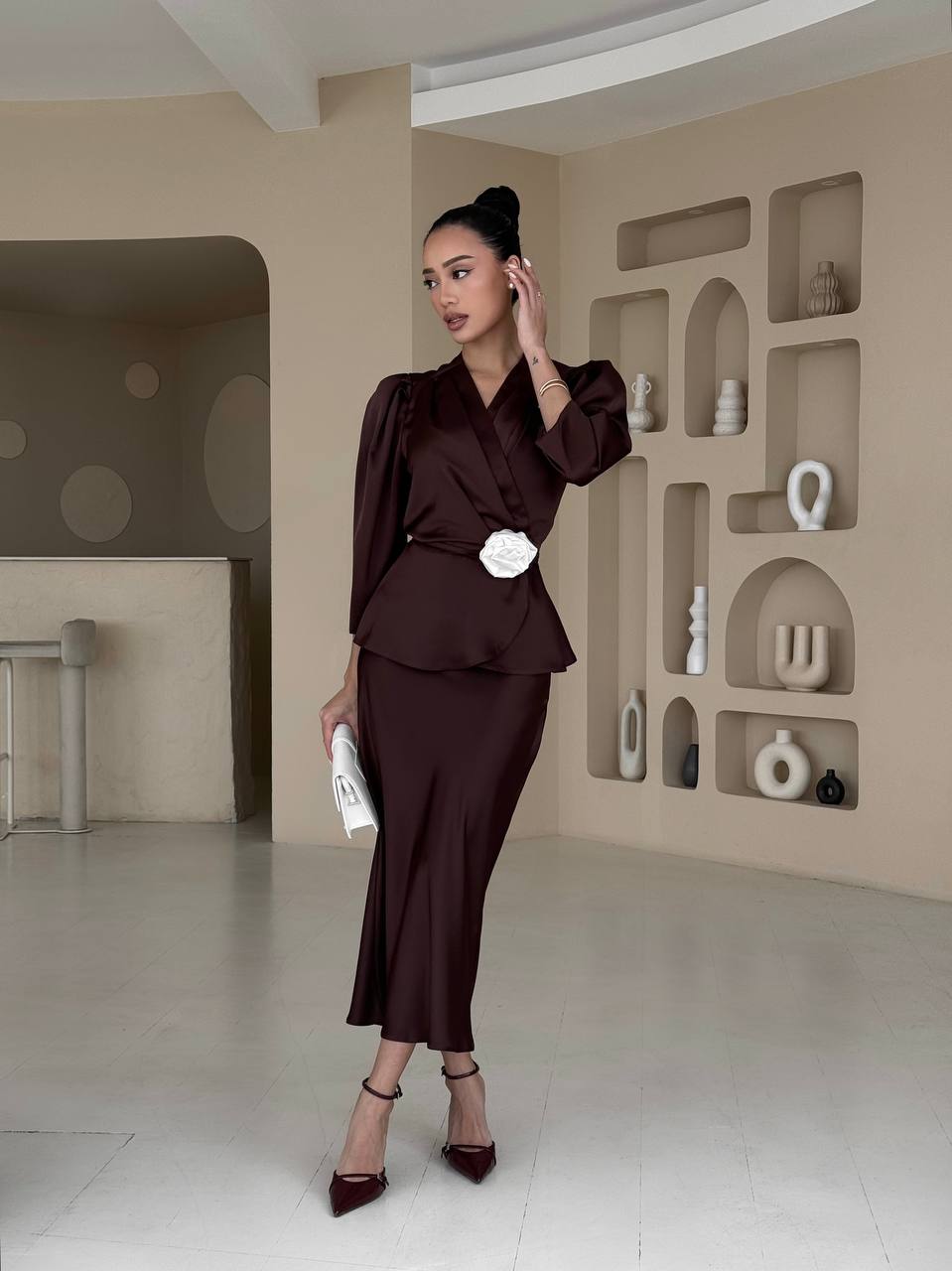 Woman in a brown outfit standing in a modern interior setting with shelves.