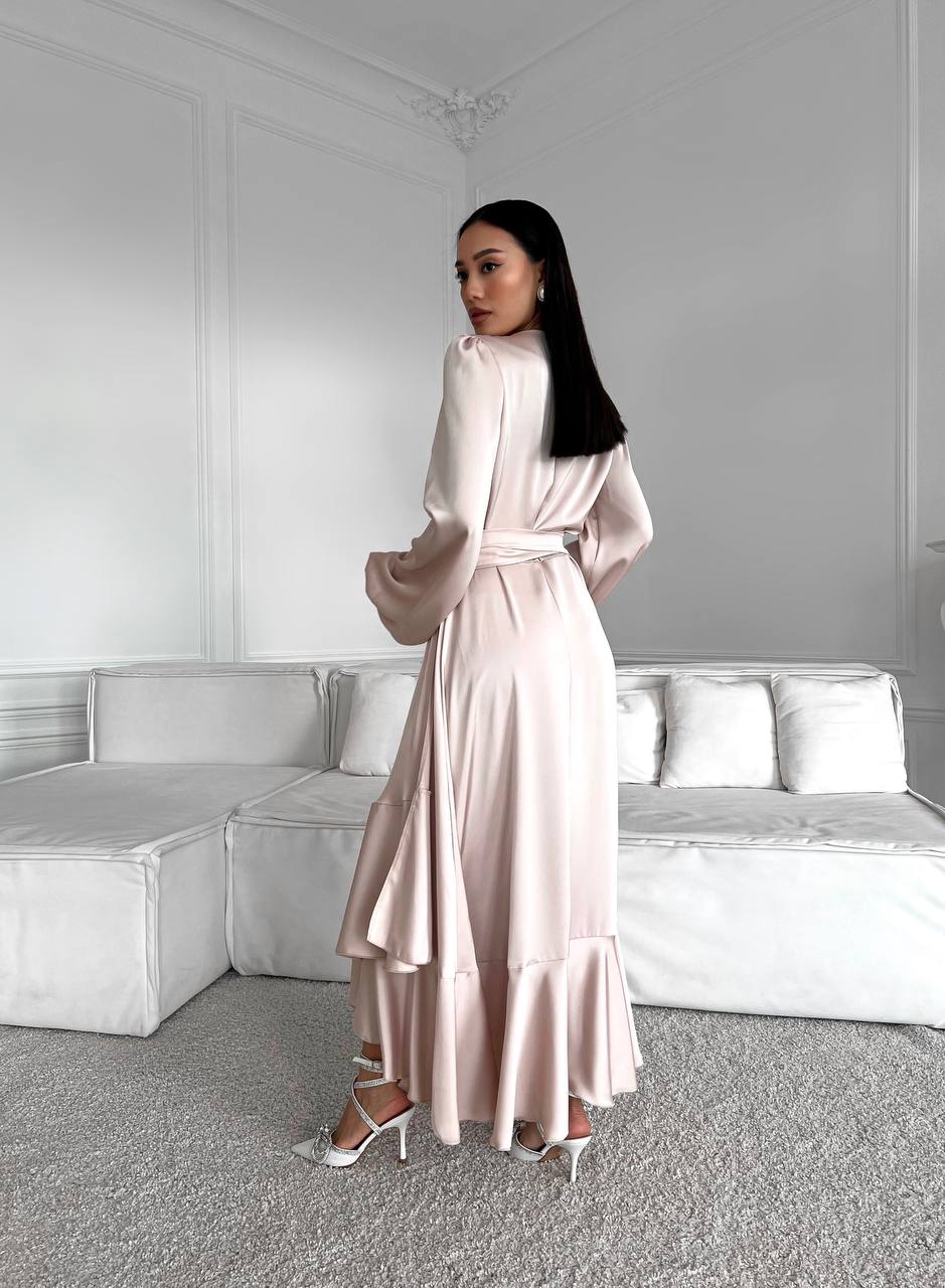 Woman in a light pink satin dress standing in a minimalistic room with white furniture.