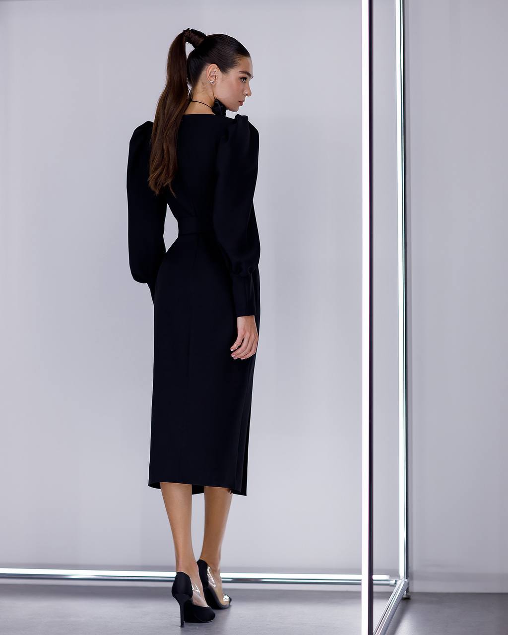 Woman wearing a black dress standing in front of a mirror on a plain background