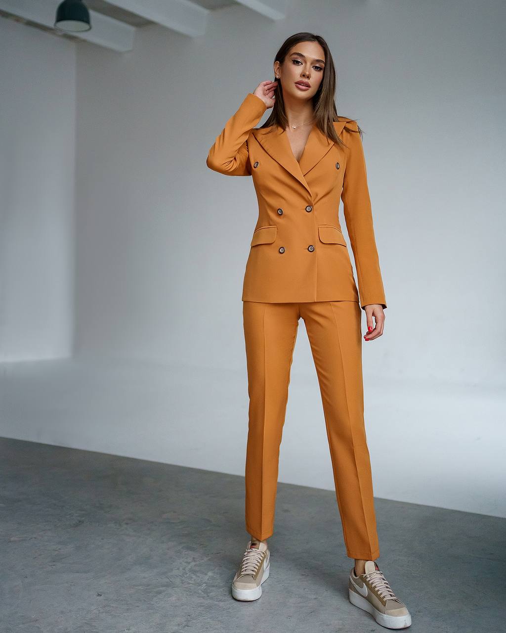 Woman wearing a mustard yellow suit standing in a minimalistic room.
