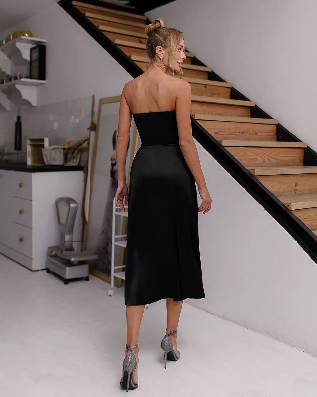 Woman in a black strapless dress standing in a modern interior setting.