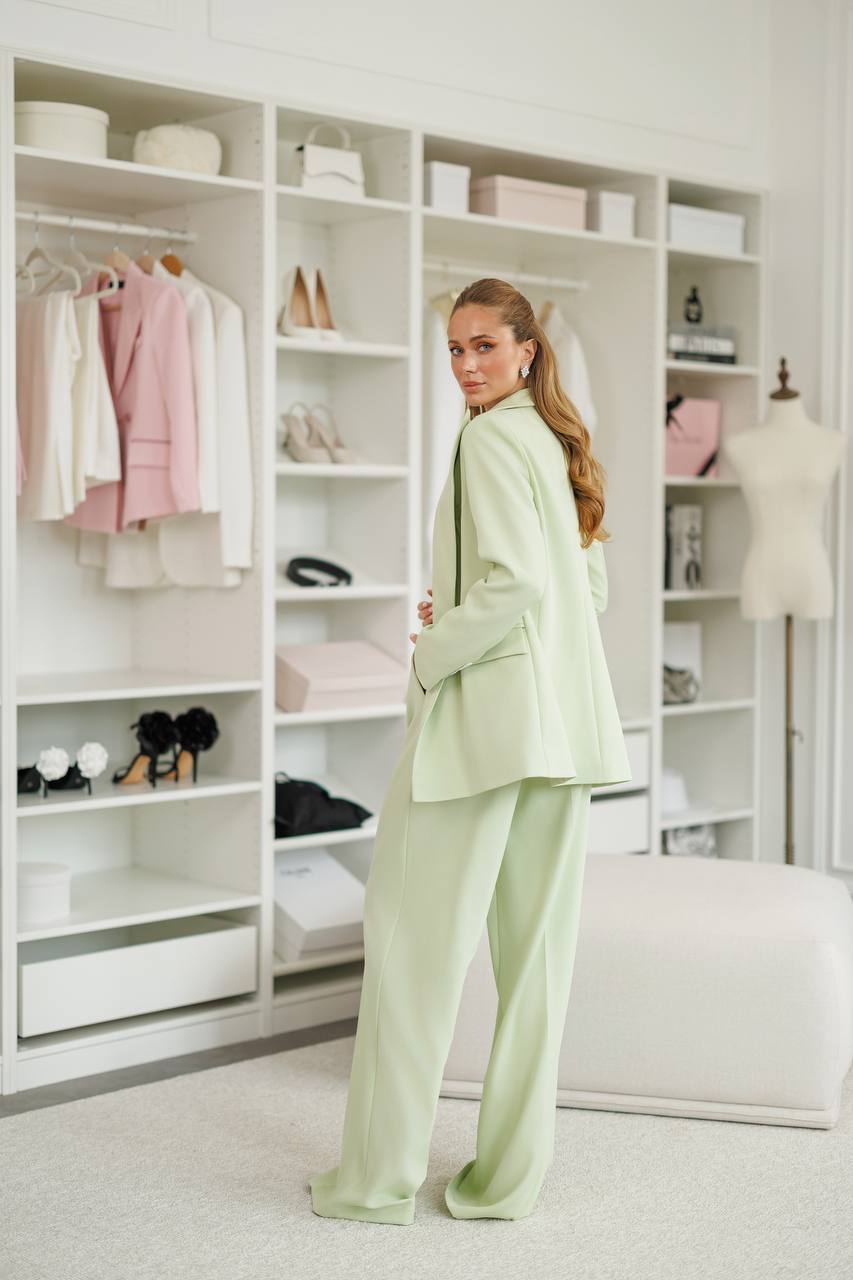 Woman in a light green suit standing in a stylishly organized closet.