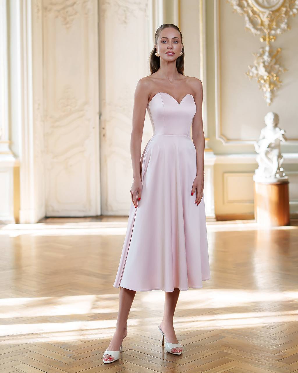 Woman wearing a strapless white dress in an elegant room with wooden floors and decorative walls.