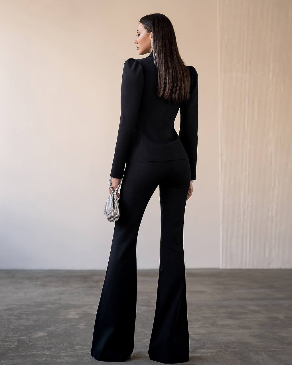 Woman wearing a black outfit with flared pants in a minimalistic setting