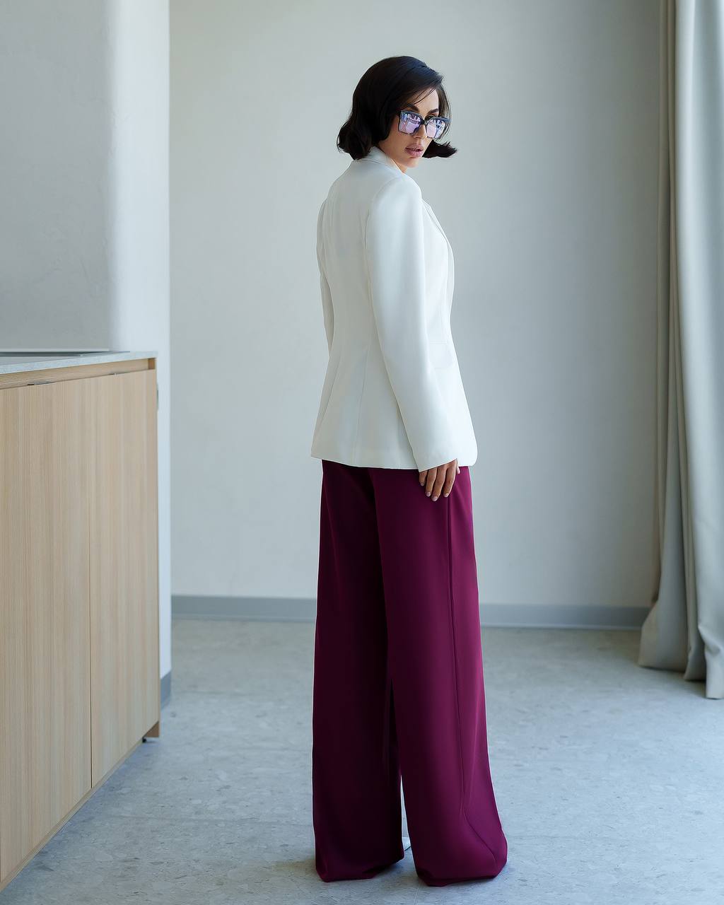 Woman wearing a white top and burgundy pants in a minimalistic room.