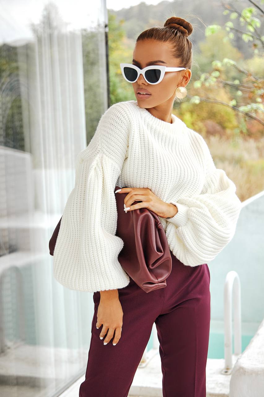 Woman wearing a white sweater and burgundy pants outdoors