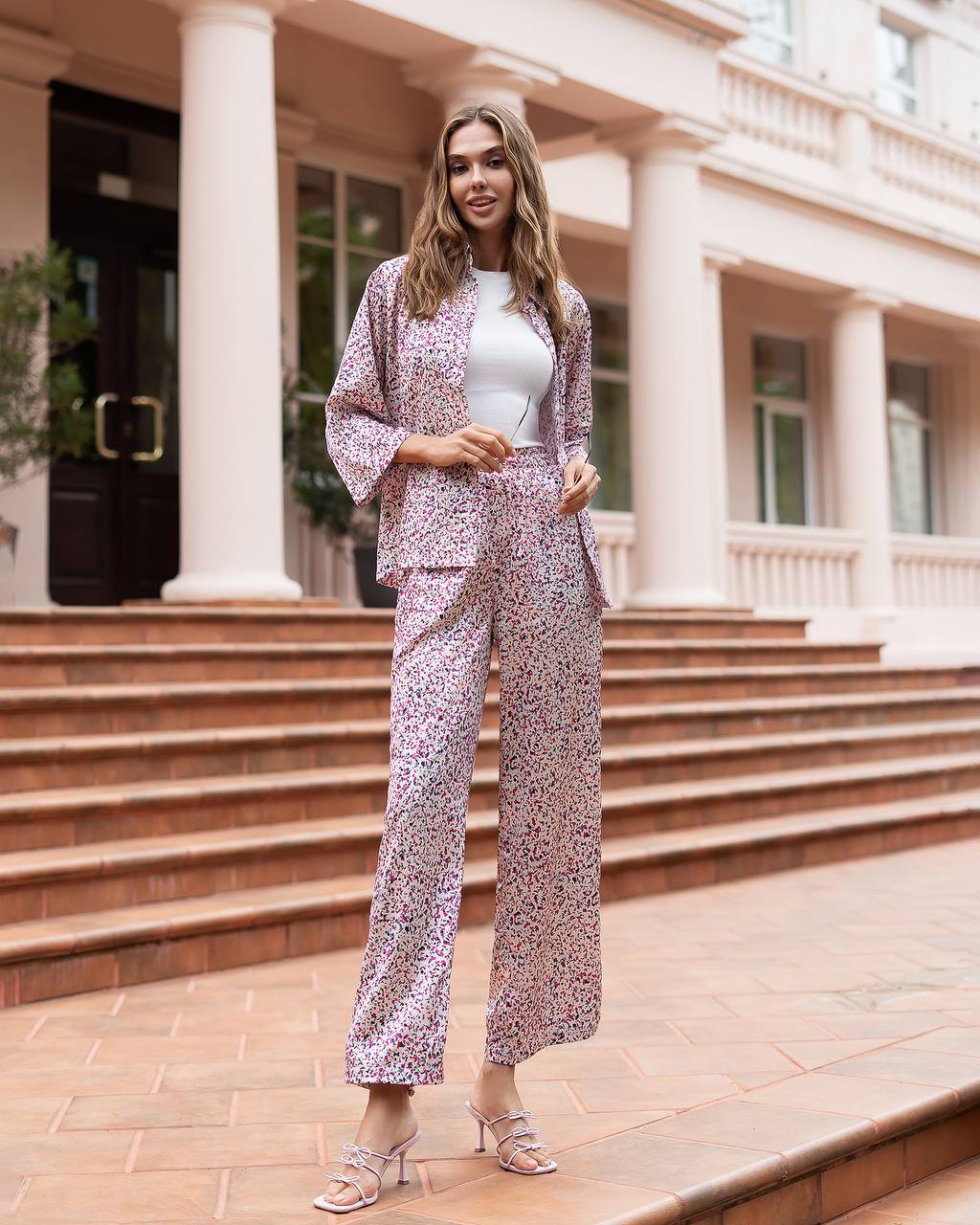 Woman in a floral outfit standing in front of a building with columns.