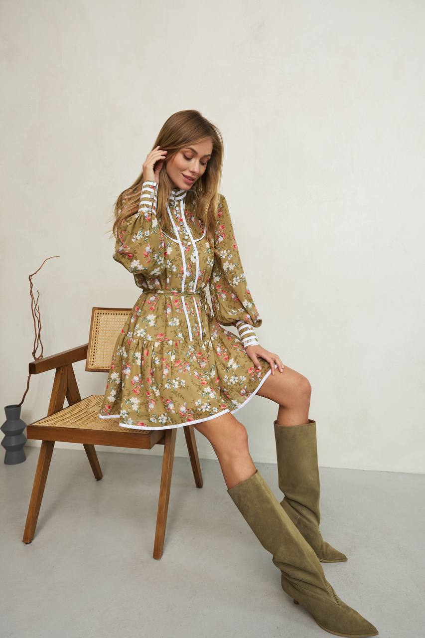 Woman in a floral dress and knee-high boots sitting on a chair against a white background
