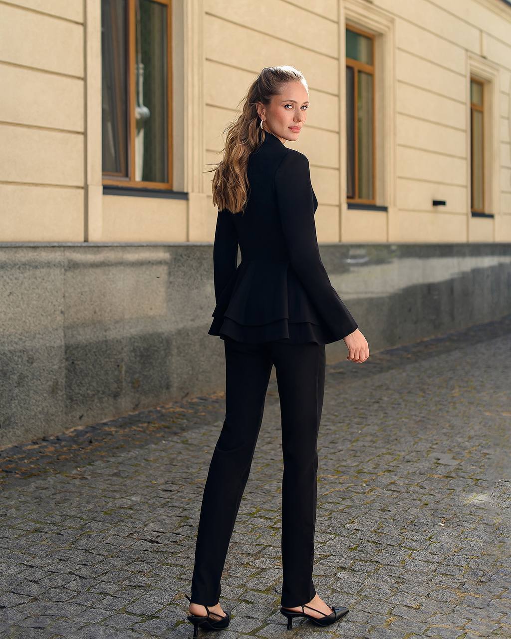 Woman in a black suit standing on a cobblestone street with a building in the background